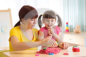Cute child girl and mother playing with kinetic sand at home