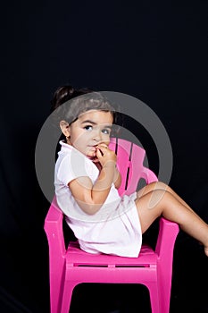 Cute child girl on pink chair seat in black background