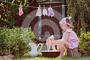 Cute child girl in pink dress playing toy wash in sunny summer garden