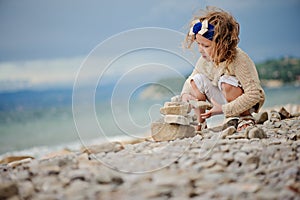 Cute child girl playing and building rock tower on summer beach