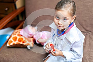 Cute child girl playing doctor with baby doll toy