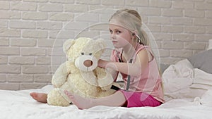 Cute child girl playing doctor with teddy bear