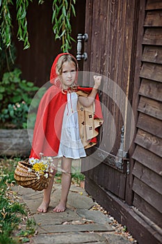 Cute child girl plays little red riding hood in summer garden