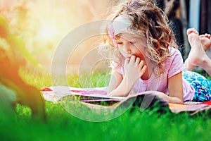 Cute child girl reading book in summer garden outdoor