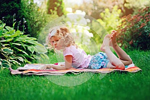 Cute child girl reading book in summer garden outdoor