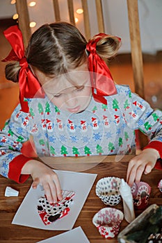 Cute child girl in seasonal sweater making christmas postcards at home