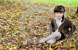 Cute child girl sitting on carpet of autumn leaves