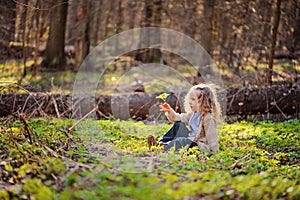 Cute child girl sitting in green leaves in early spring forest