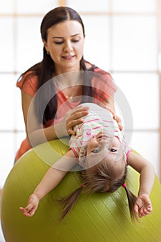 Cute child girl stretching on pilates fitness ball with mom in gym