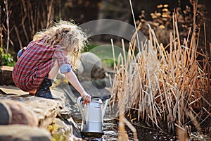 Cute child girl with watering can gathering water from pond
