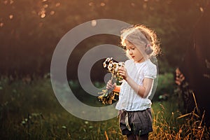 Cute child girl with wild flowers on summer sunset field