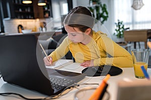 Cute child with headphones using laptop computer for online learning. Home school. Girl doing homework at home