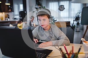 Cute child with headphones using laptop computer for online learning. Home school. Girl doing homework at home