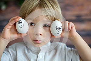 Cute child, holding white eggs with emotions drawn on them, funny faces