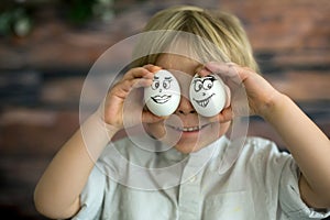 Cute child, holding white eggs with emotions drawn on them, funny faces