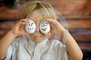 Cute child, holding white eggs with emotions drawn on them, funny faces