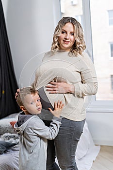 Cute child hugging belly pregnant mother New life and pregnancy concept Little boy embrace big belly mom Waiting for brother