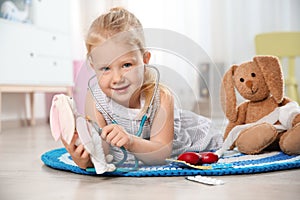 Cute child imagining herself as doctor while playing with stethoscope and toy bunny