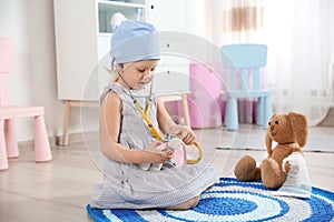 Cute child imagining herself as doctor while playing with stethoscope and toy bunny