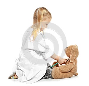 Cute child imagining herself as doctor while playing with stethoscope and toy bunny on white background