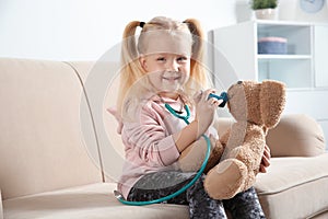 Cute child imagining herself as doctor while playing with toy bunny on couch
