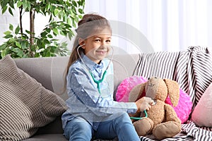 Cute child imagining herself doctor while playing with stethoscope on sofa