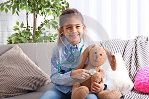 Cute child imagining herself doctor while playing with stethoscope on sofa