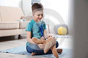 Cute child imagining himself as doctor while playing with stethoscope and toy bunny