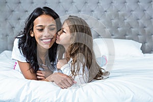 Cute child kissing her mother on the bed