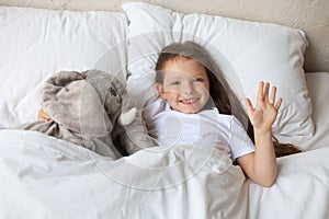 Cute child little girl wake up and lies in the bed with a toy elephant