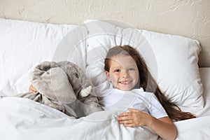 Cute child little girl wake up and lies in the bed with a toy elephant