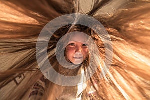 A cute child with long hair like a lion`s mane looks down. Children`s portrait wide-angle photo.Portrait of a cheerful little gi