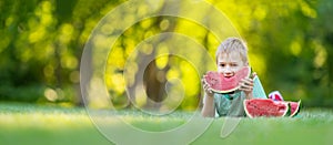 Cute child lying on the grass and eating juicy slice of watermelon.