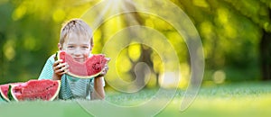 Cute child lying on the grass and eating juicy slice of watermelon.