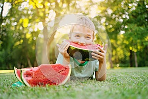 Cute child lying on the grass and eating juicy slice of watermelon.