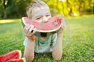 Cute child lying on the grass and eating juicy slice of watermelon.