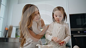 Cute child making apple pie with mommy at home. Mother straightens daughter hair