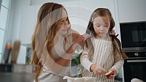 Cute child making apple pie with mommy at home. Mother straightens daughter hair
