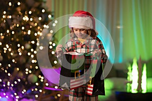 Cute child opening gift bag in room decorated for night Christmas. Merry Christmas and Happy New Year. Kid celebrating
