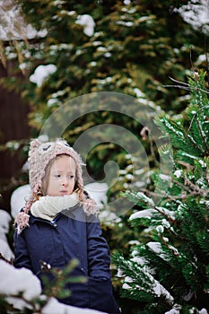 Cute child in owl knitted hat on the walk in winter snowy garden