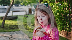 cute child in a pink jacket eating a hot dog outdoors