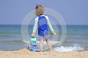 Cute child playing with car truck on sandy beach. Happy sailor boy on coast looking to the sea