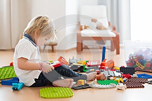 Cute child, playing with colorful toy blocks. Little boy building house of block toys sitting on the floor in sunny spacious