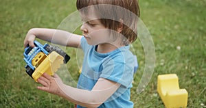 Cute child is playing with toy car and cubes on green grass. Portrait close up