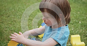 Cute child is playing with toy car and cubes on green grass. Portrait close up