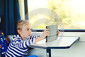 Cute child playing video games online on tablet during trip. Kid travels on a train