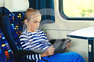 Cute child playing video games online on tablet during trip. Kid travels on a train