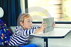 Cute child playing video games online on tablet during trip. Kid travels on a train