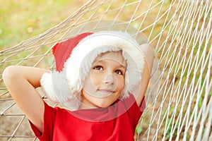 Cute child in santa hat and resting on hammock. Little boy dreaming about christmas gifts. Christmas family vacation at tropical