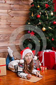 Cute child in Santa hat writes letter to Santa near christmas tree